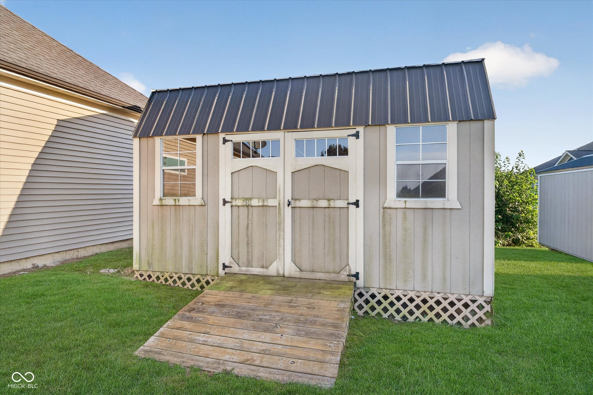 Storage shed featuring a metal roof, double entry doors, two windows, and a wood ramp