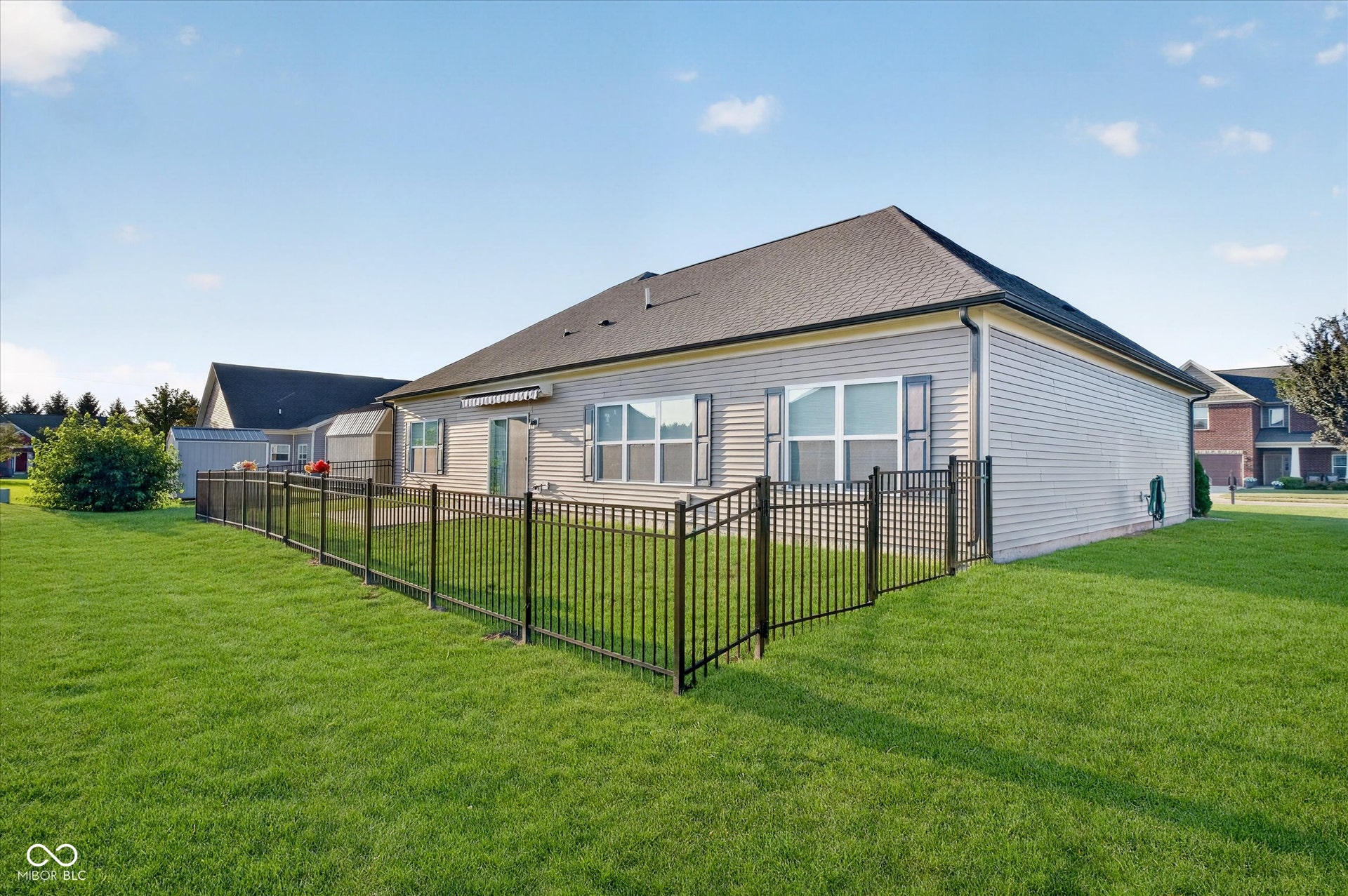 Expansive grassy yard with black metal fencing, a concrete patio, and light-colored siding