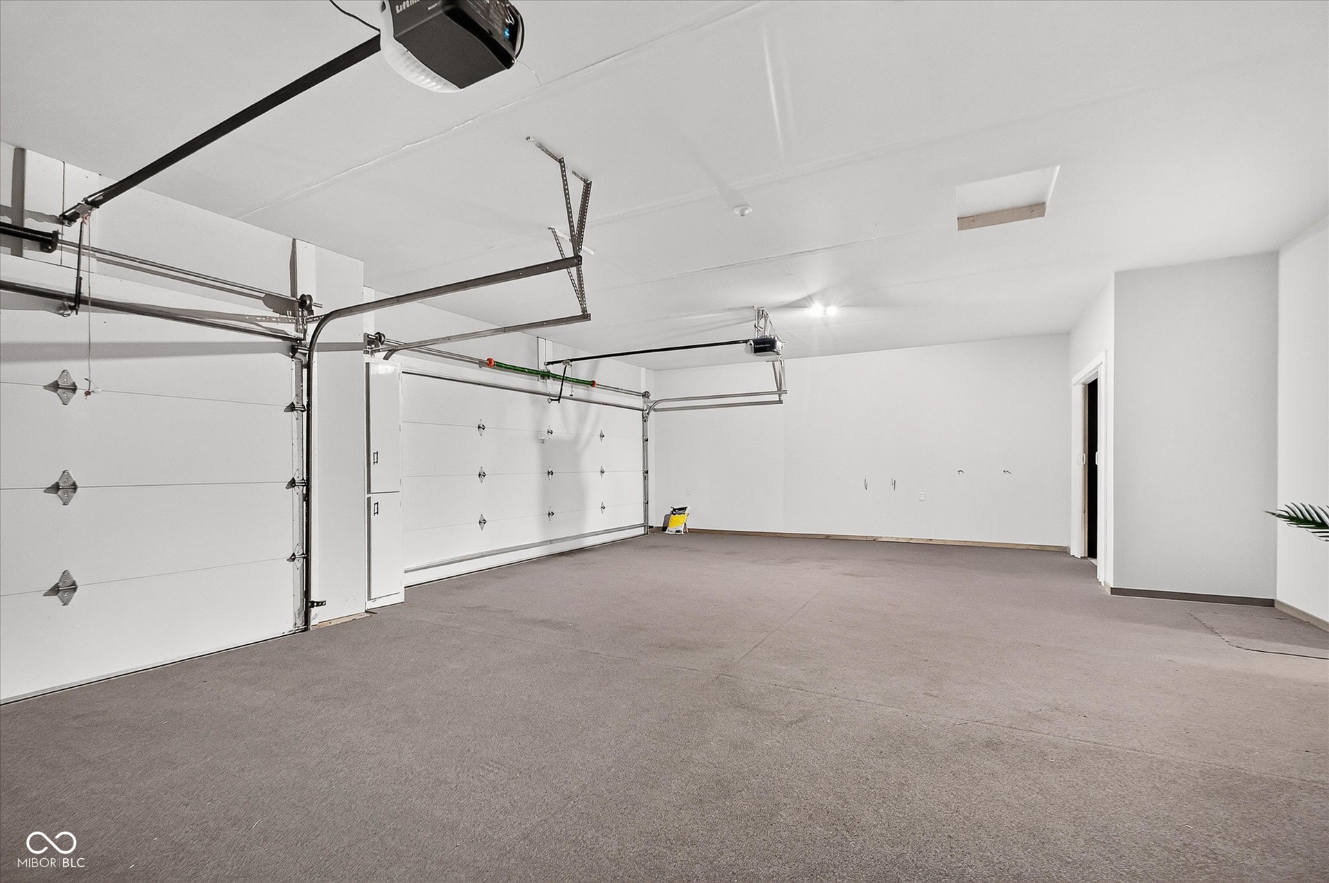 Carpeted garage with multiple overhead doors and an overhead garage door opener