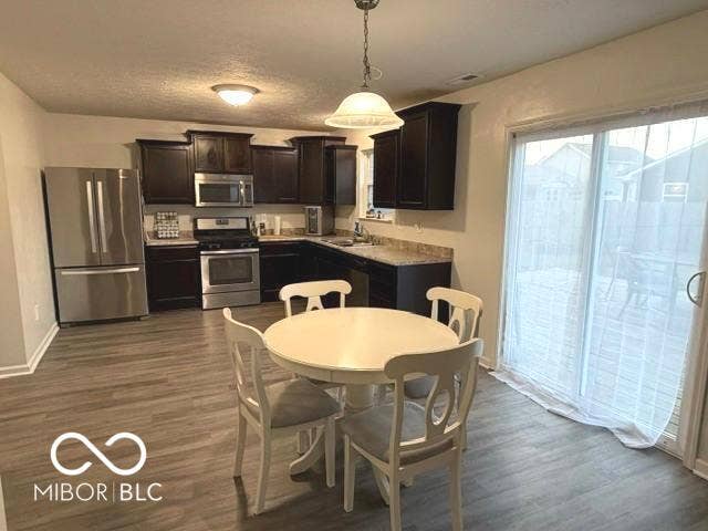 Large kitchen featuring dark wood cabinetry, stainless steel appliances, granite-style countertops, wood-finish flooring, and a sliding glass door