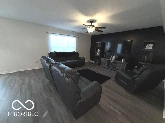 Wood-finish flooring, ceiling fan with integrated lighting, white window treatments, and a contrasting accent wall