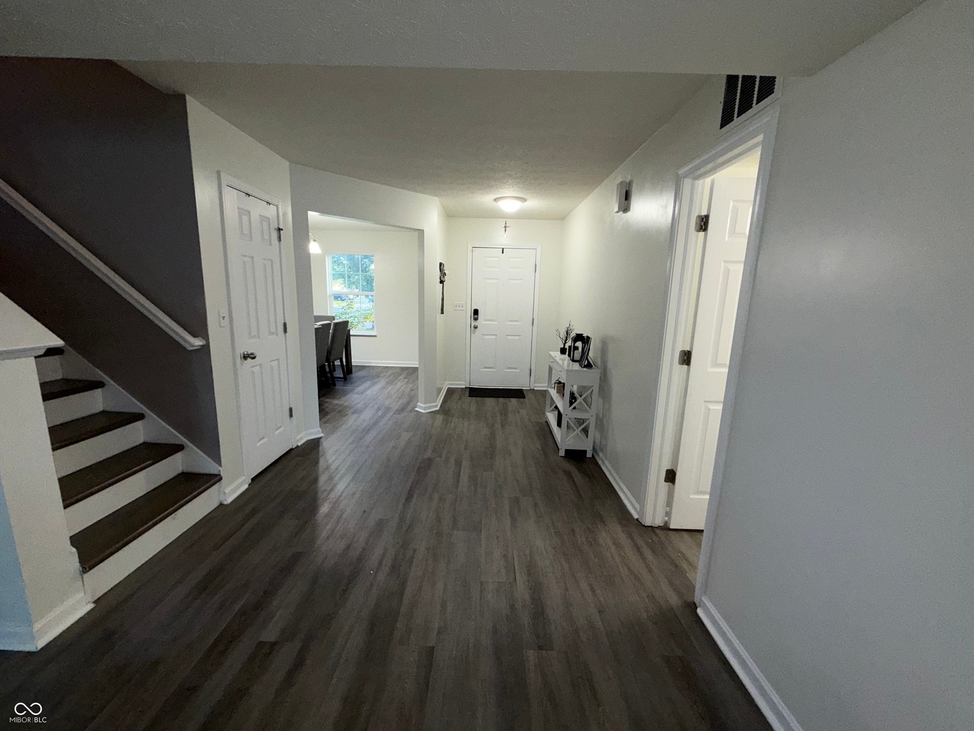 Spacious entry foyer featuring wood-finish flooring, a white paneled front door, and lamniated staircase with white risers and dark treads