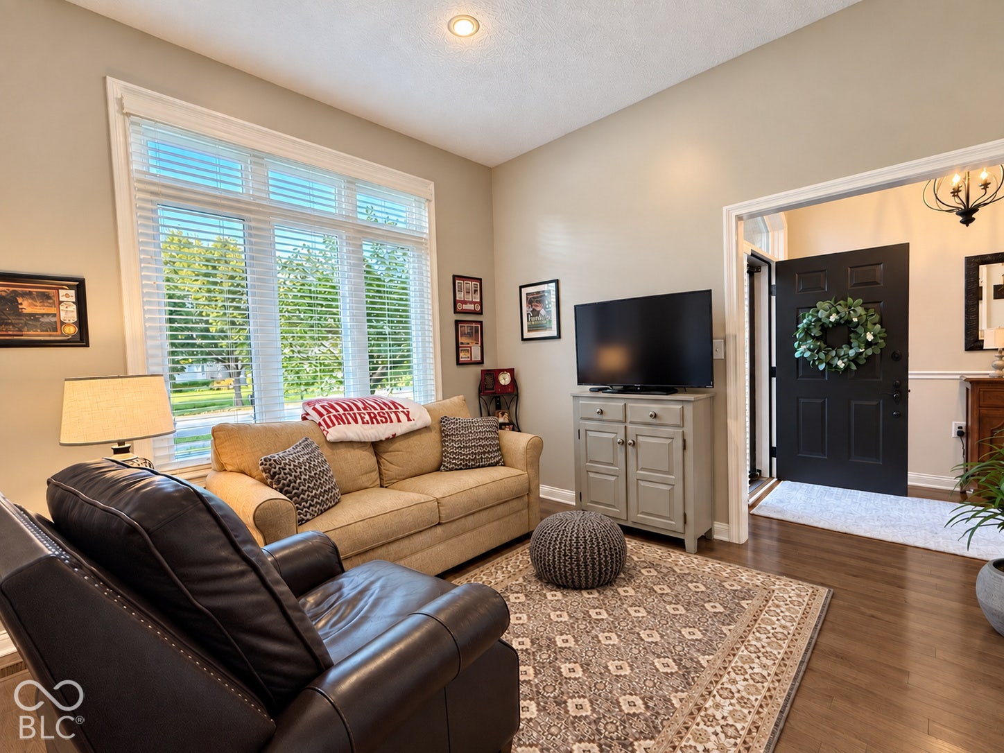 Virtually Altered - Expansive window with white blinds, recessed ceiling lighting, wood-finish flooring, and a decorative front door