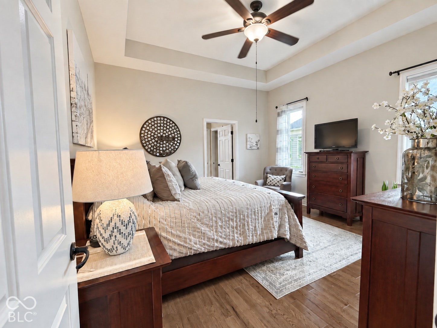 Tray ceiling with a ceiling fan light fixture, recessed windows, and wood-finish flooring