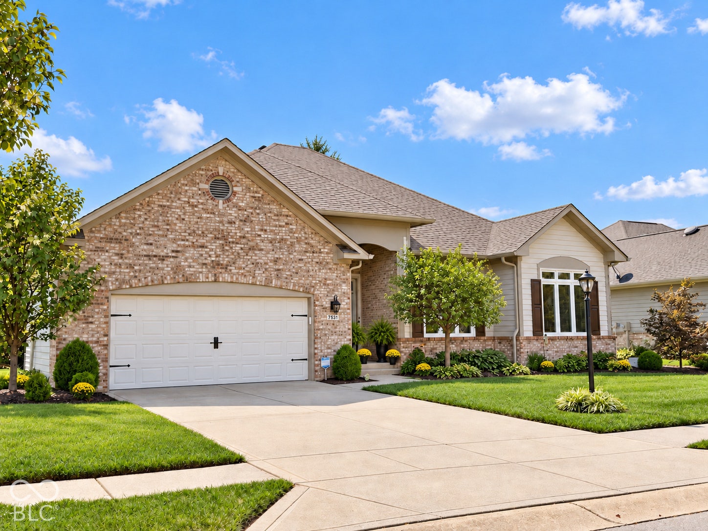 Brick and siding exterior with a concrete driveway, attached two-car garage, and established landscaping