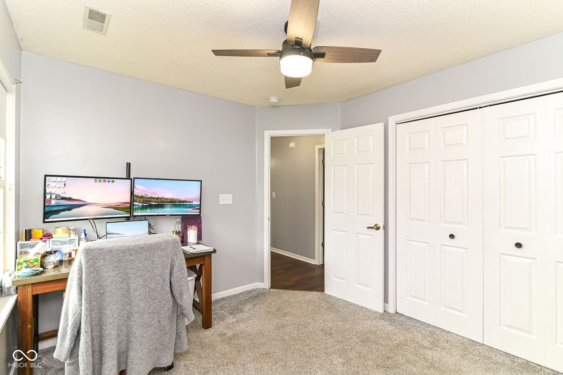 Light gray wall paint, textured ceiling, ceiling fan with light, white paneled bifold closet doors, and light gray carpet flooring