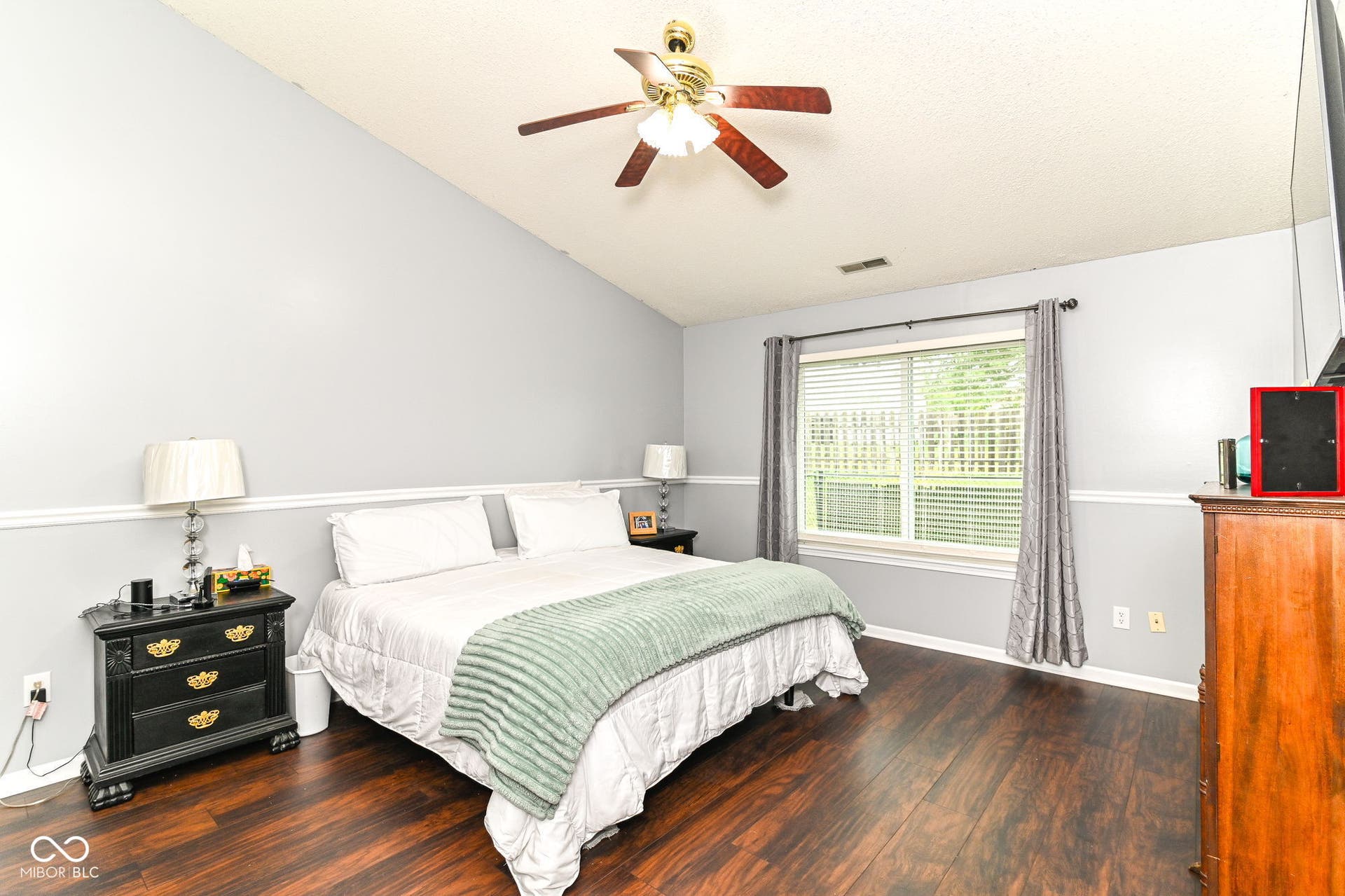 Vaulted ceiling with a ceiling fan, wood-finish flooring, two-tone wall treatment, and a window with blinds and drapes