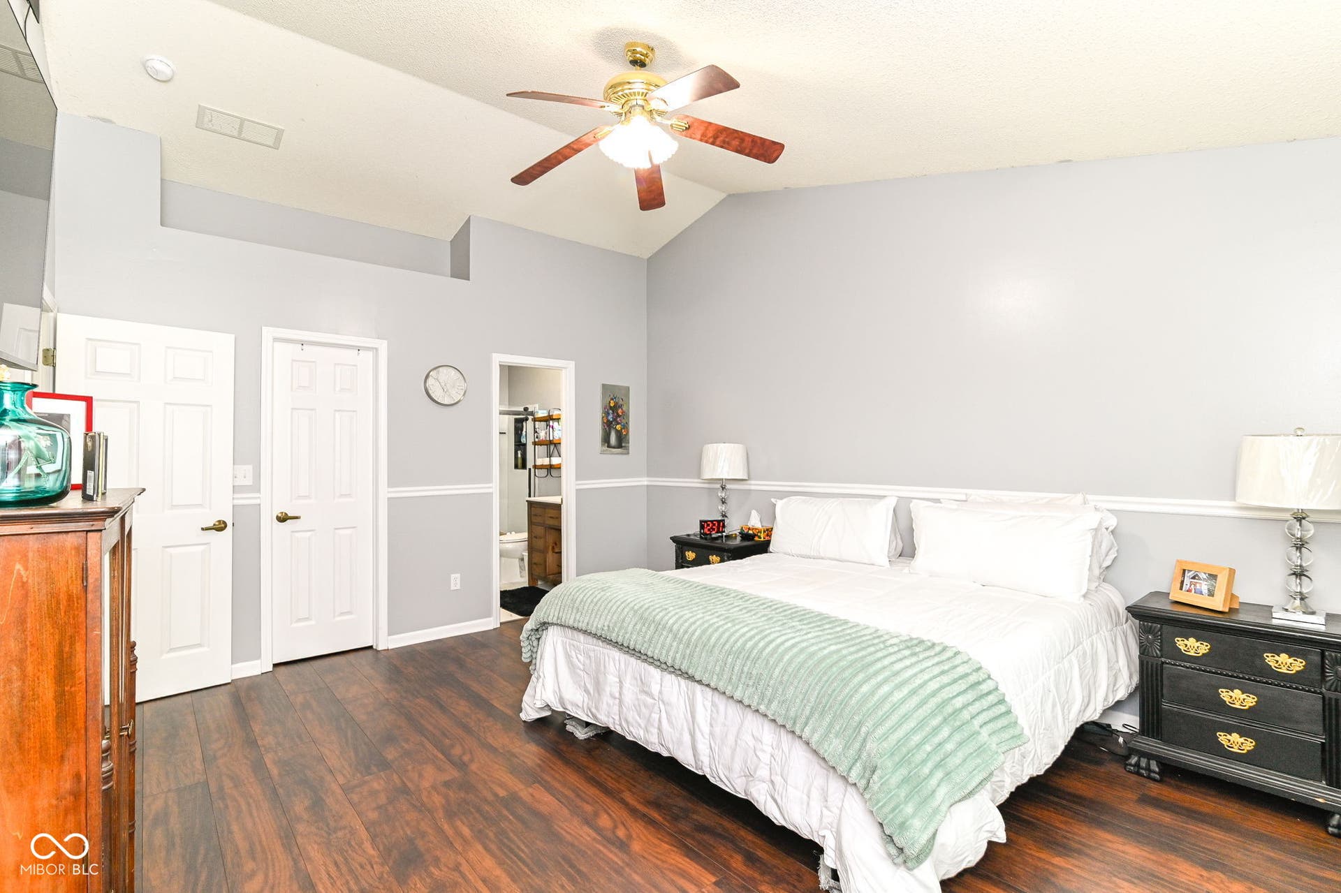Vaulted ceiling with a ceiling fan, wood-finish flooring, two-panel interior doors, and a two-tone wall finish with chair rail molding