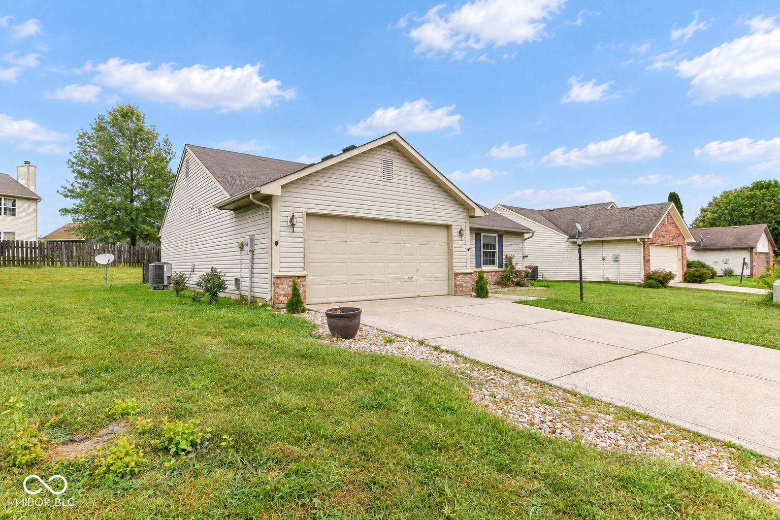 Siding exterior with brick accents, attached garage, concrete driveway, and a spacious lawn