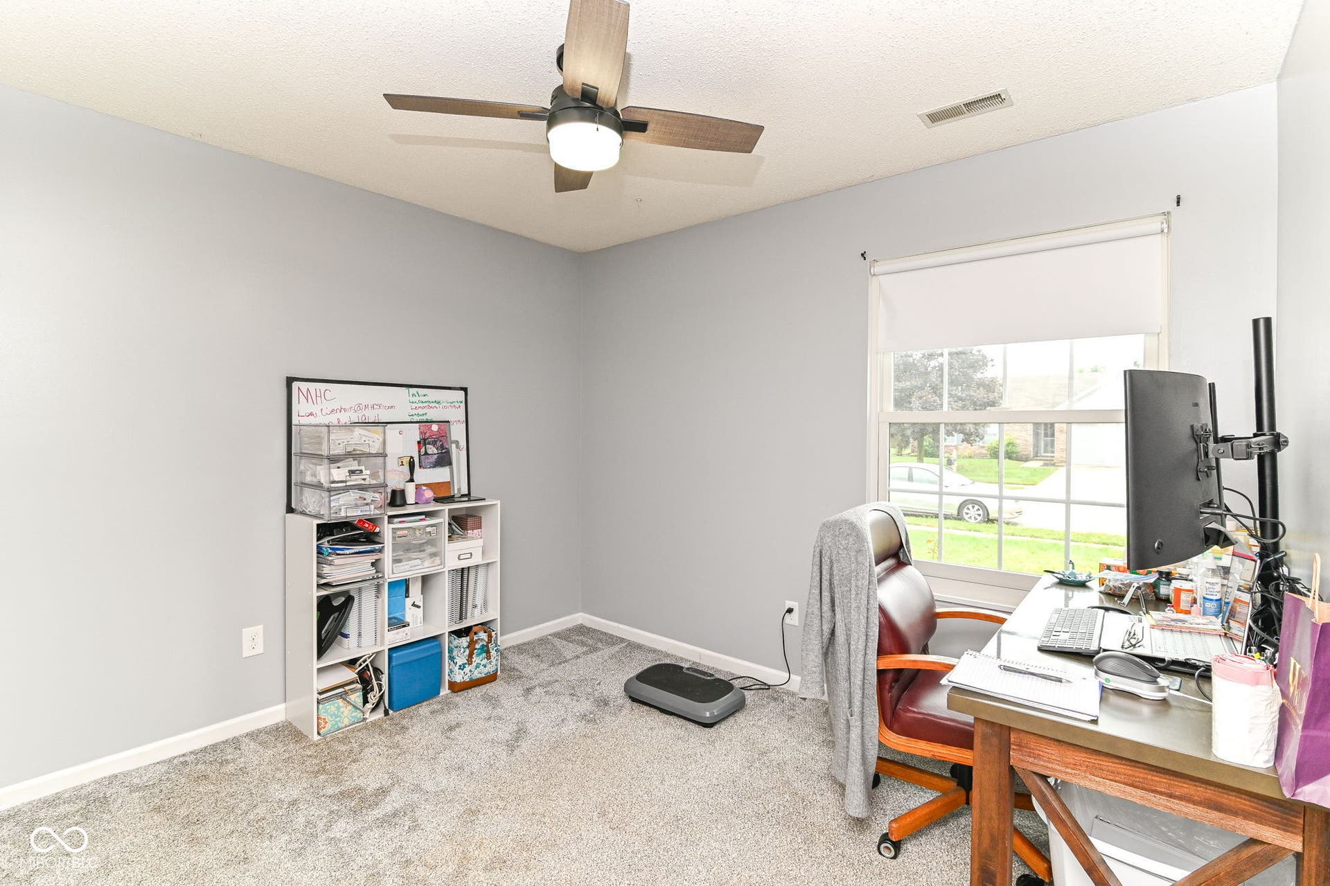 Neutral wall paint, ceiling fan with integrated lighting, window with roller shade, and carpeted flooring