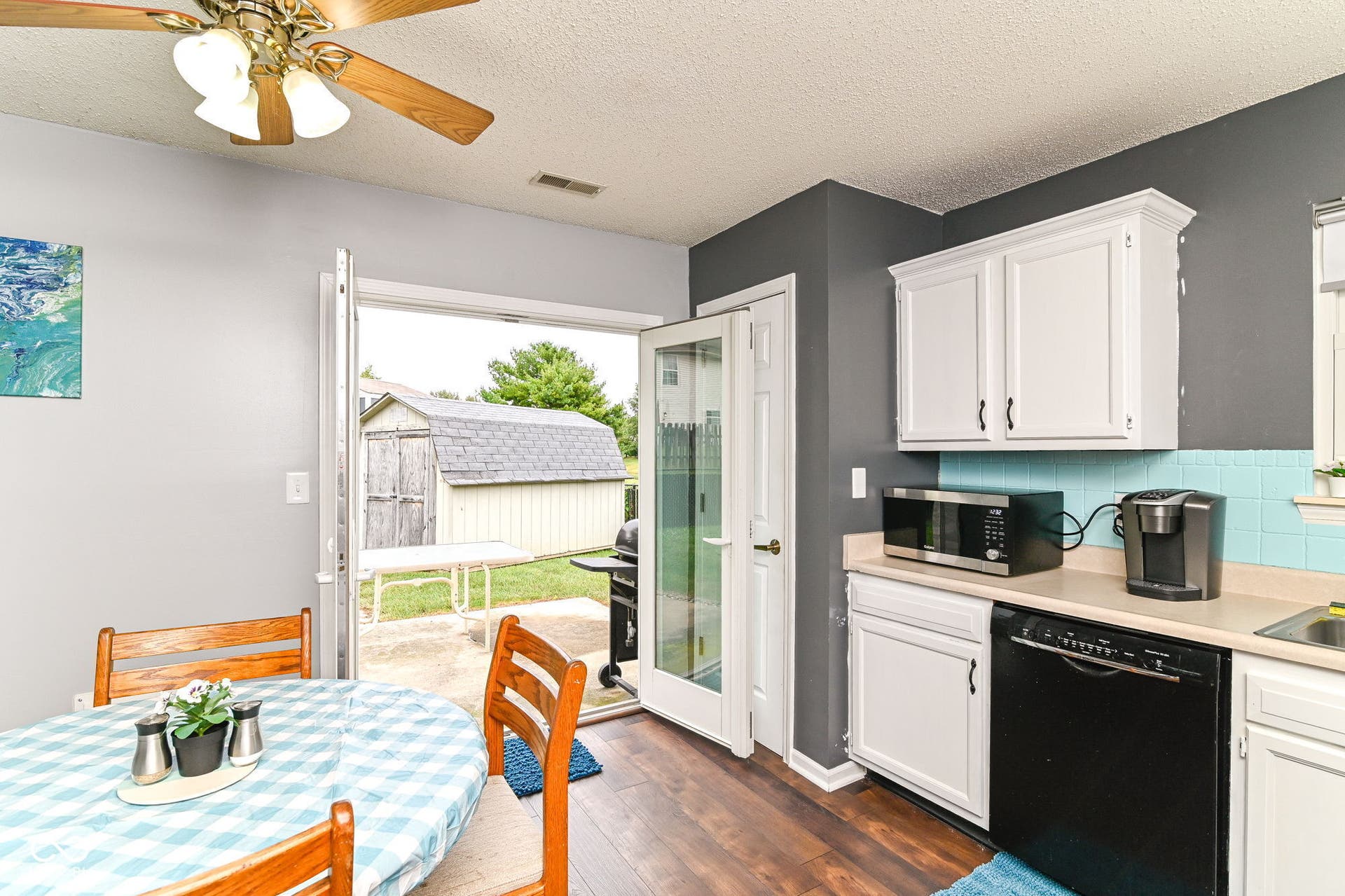 Wood-finish flooring, white cabinetry, blue tiled backsplash, and a ceiling fan with light fixture