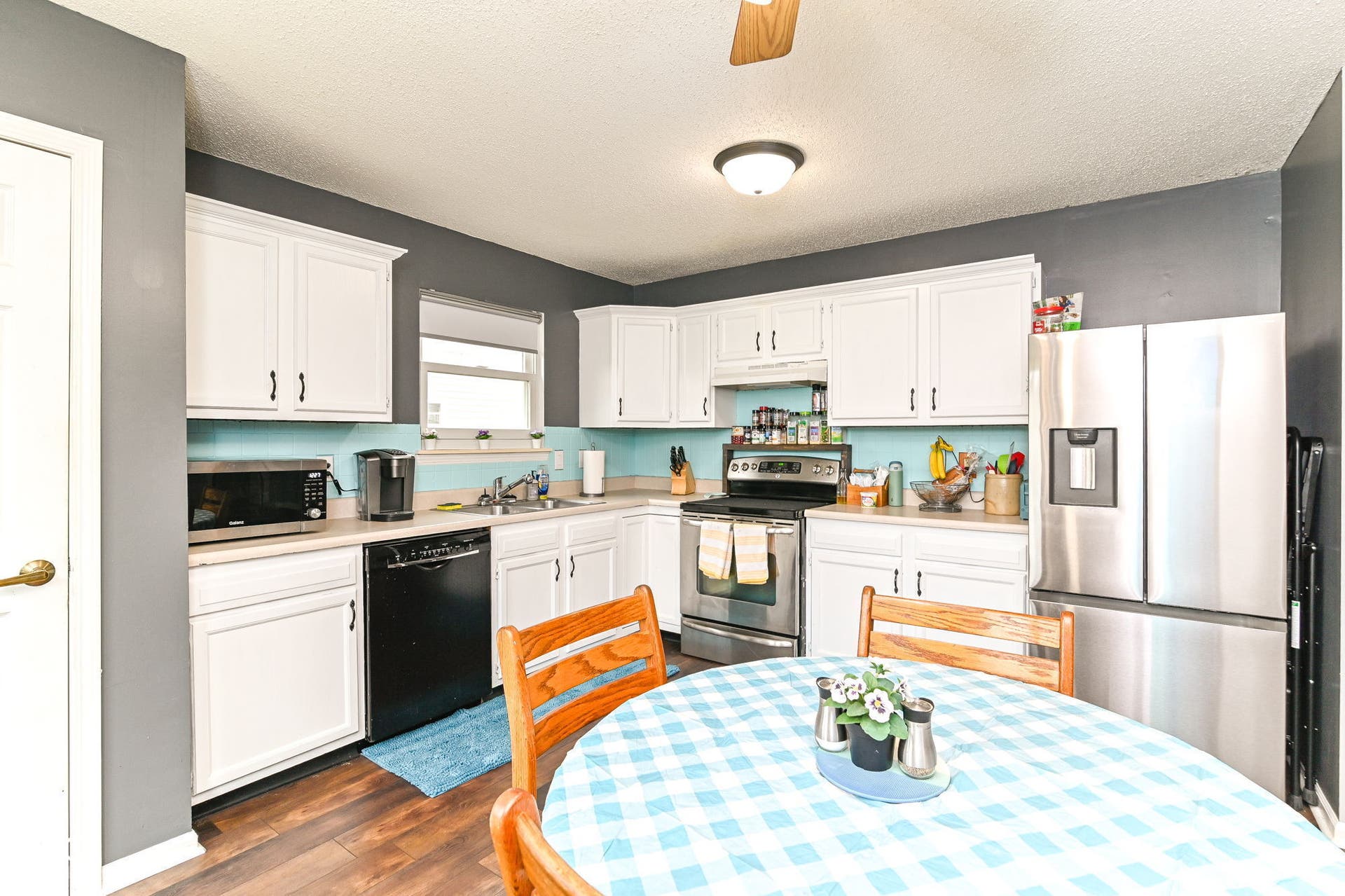 Kitchen featuring white cabinetry, black and stainless steel appliances, wood-finish flooring, and a window