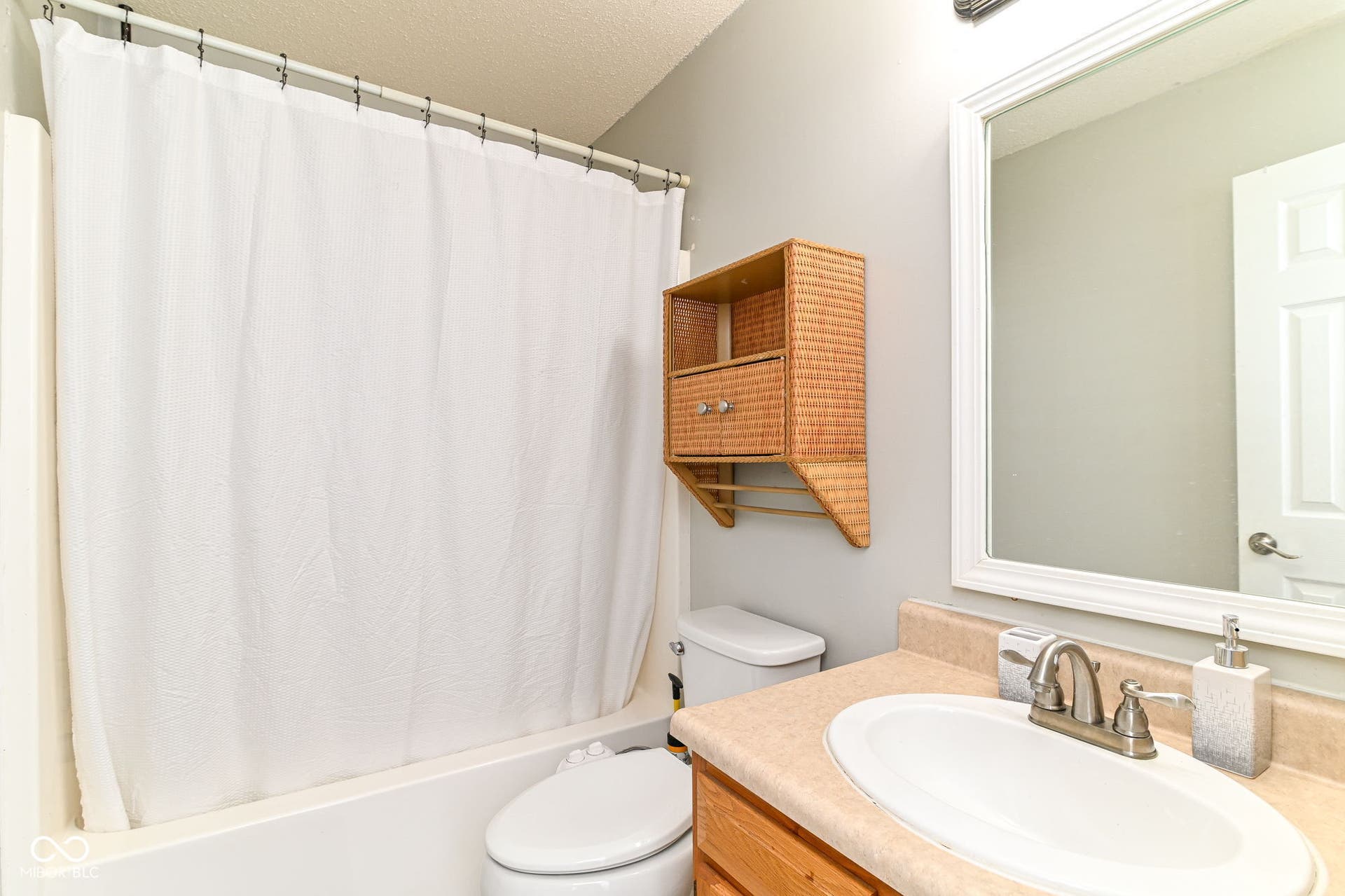 Bathroom with a white bathtub and shower surround, a vanity with an integrated sink and brushed nickel faucet, and a framed mirror
