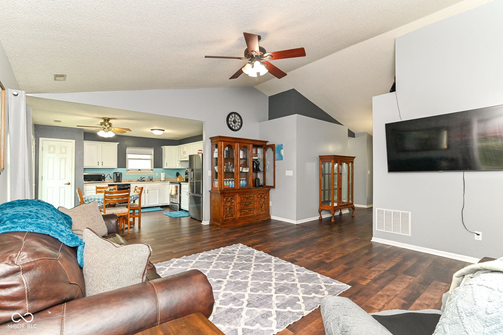 Vented vaulted ceilings with a ceiling fan, wood-finish flooring, and white kitchen cabinetry
