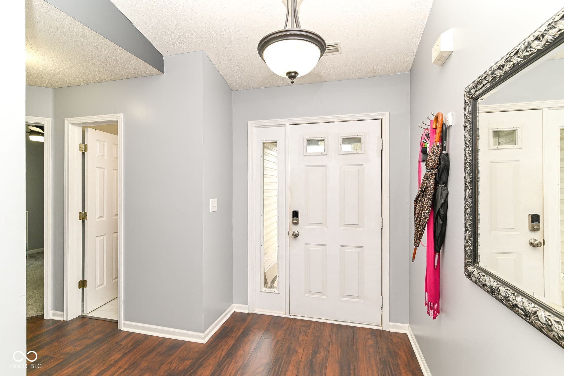 Hardwood-finish flooring throughout the entry, featuring a paneled door with glass inserts and an overhead drum light fixture
