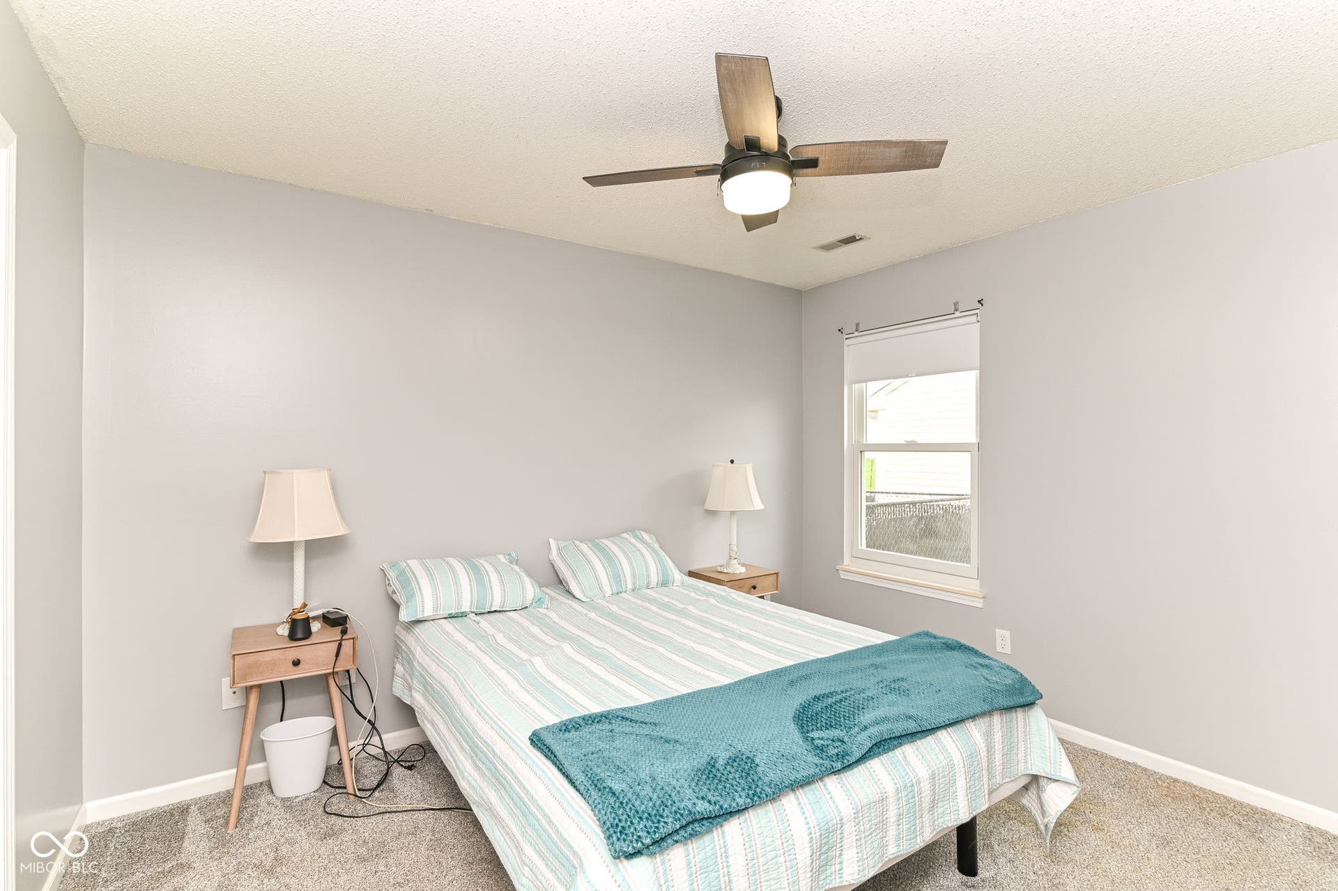 Window with roller shade, ceiling fan with integrated lighting, textured ceiling, and light gray wall finish