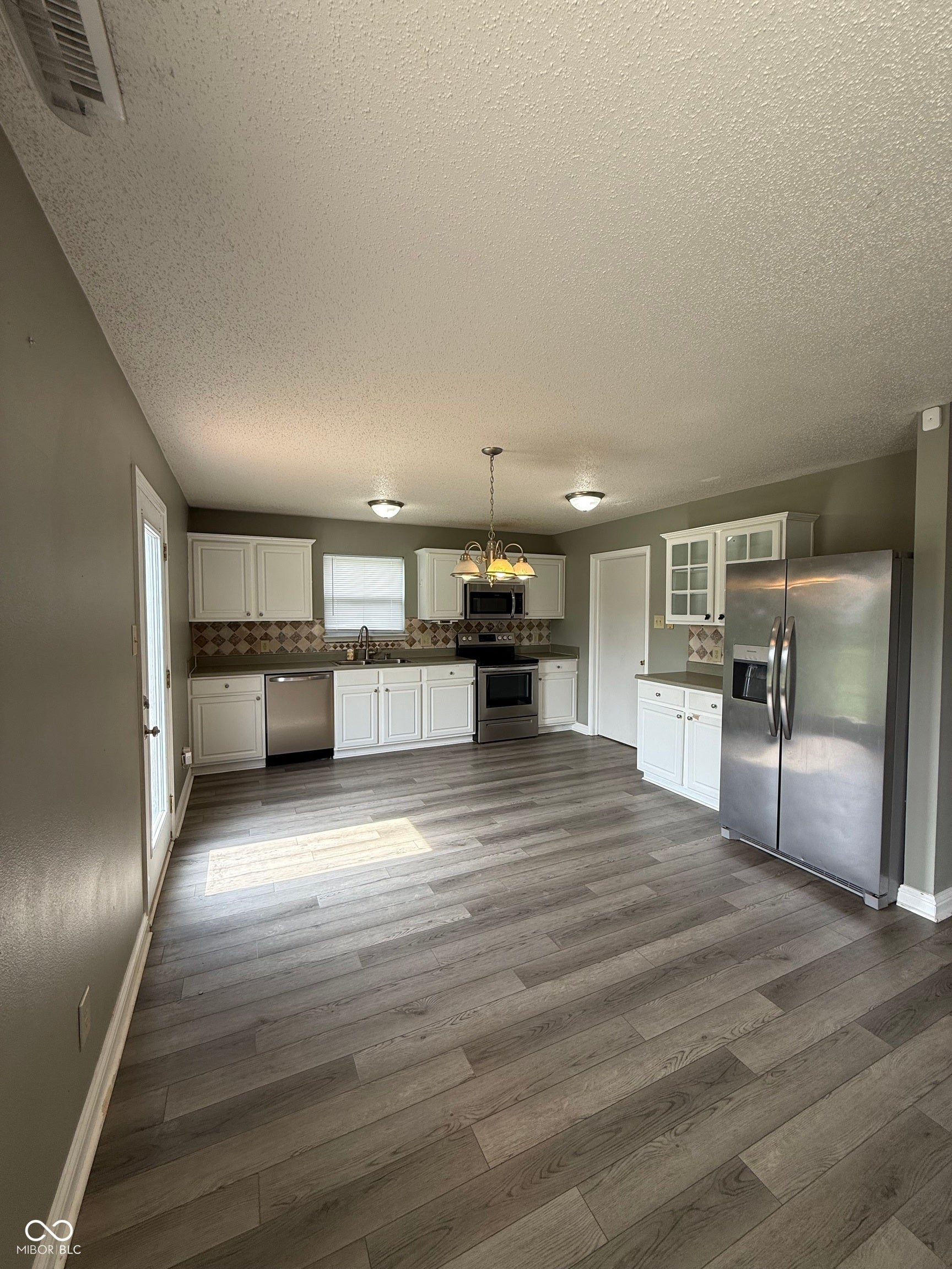 6235 E Mariah Hill Lane, Camby, IN 46113 Expansive kitchen featuring white cabinetry, stainless steel appliances, patterned backsplash, wood-finish flooring, and a chandelier