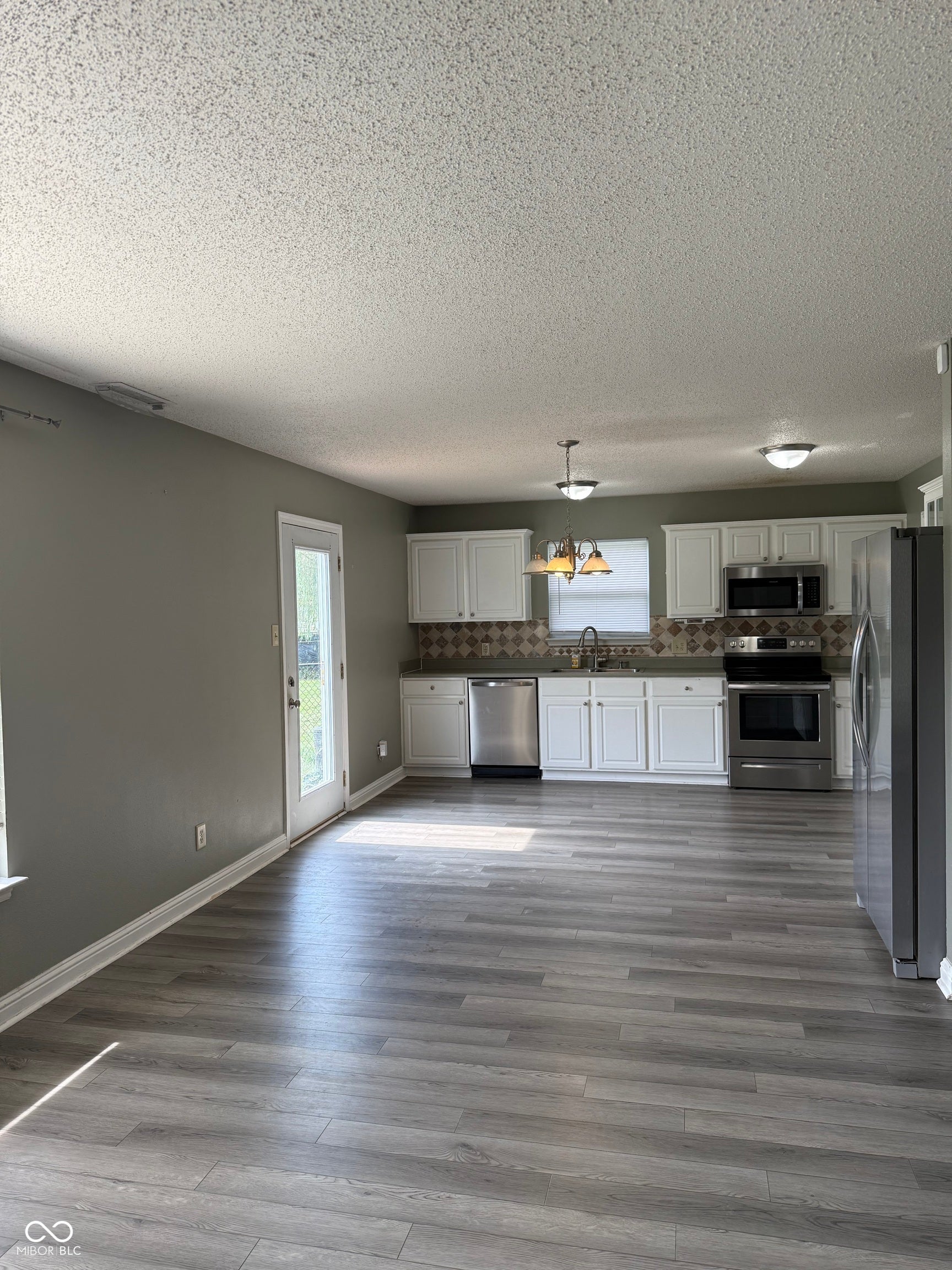 6235 E Mariah Hill Lane, Camby, IN 46113 Open-concept kitchen and living area featuring white cabinetry, stainless steel appliances, wood-finish flooring throughout, and abundant natural light from multiple windows and glass door access
