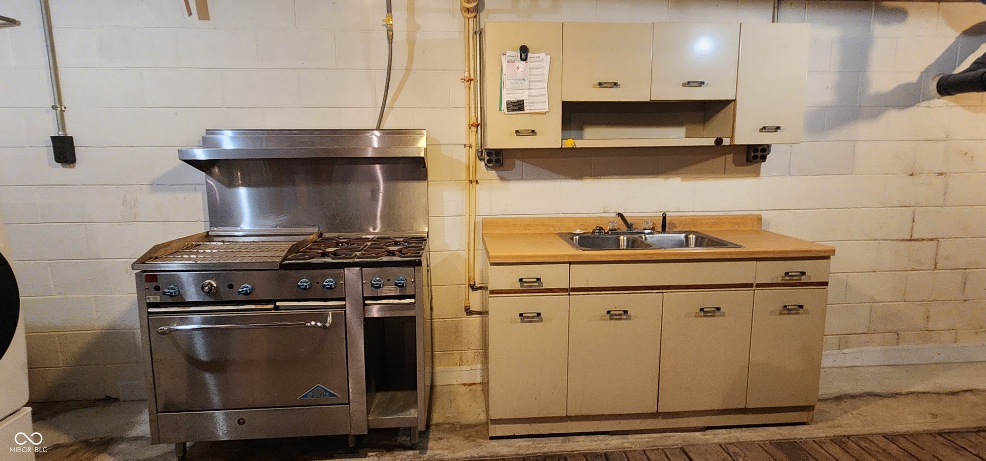 Basement kitchen area with stainless steel range with integrated griddle and hood, accompanied by a utility sink, light-toned cabinetry, and wood-finish flooring