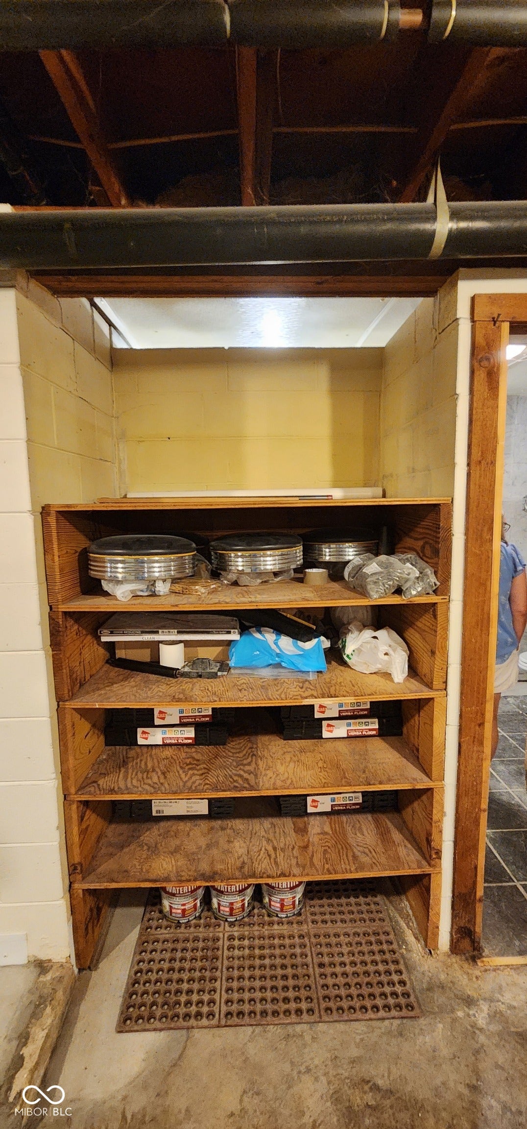 Built-in wooden shelving within a recessed alcove, featuring a concrete floor and exposed ceiling joists