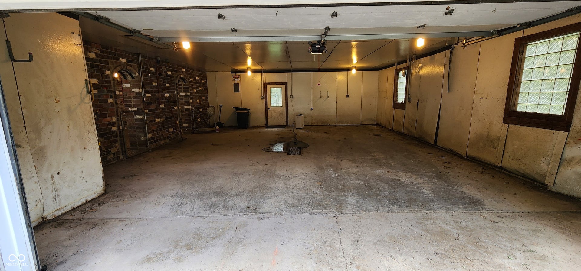 Spacious garage with exposed brick accents, block glass windows, and multiple overhead light fixtures
