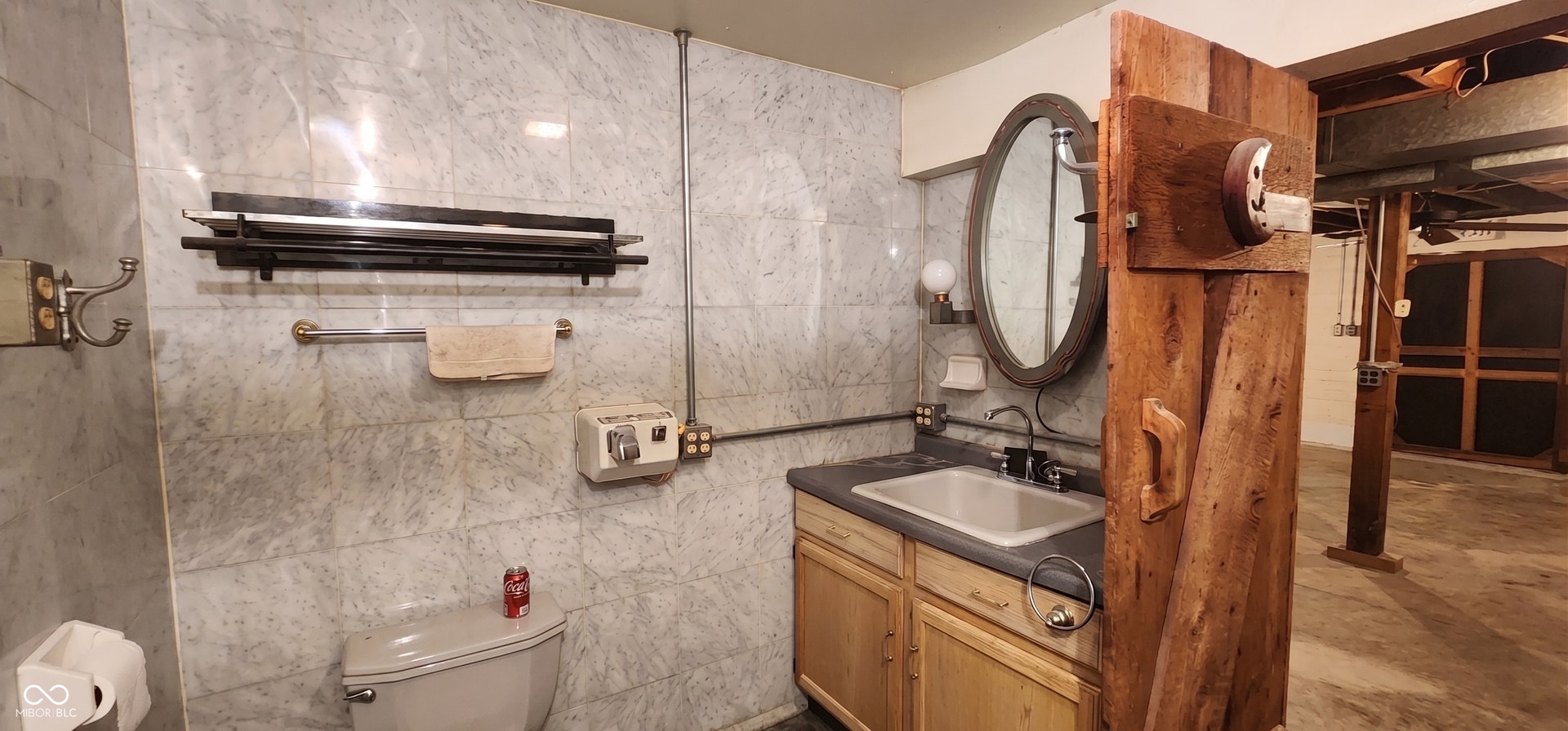 Marble-look wall tile, wood-finish vanity with countertop, oval mirror, and exposed conduit