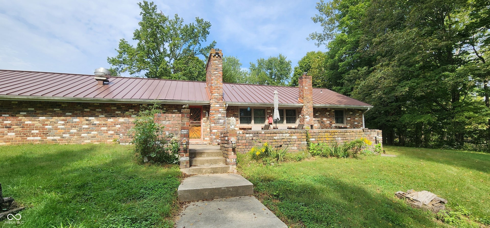 Brick exterior with a metal roof, front concrete steps, and a raised patio area