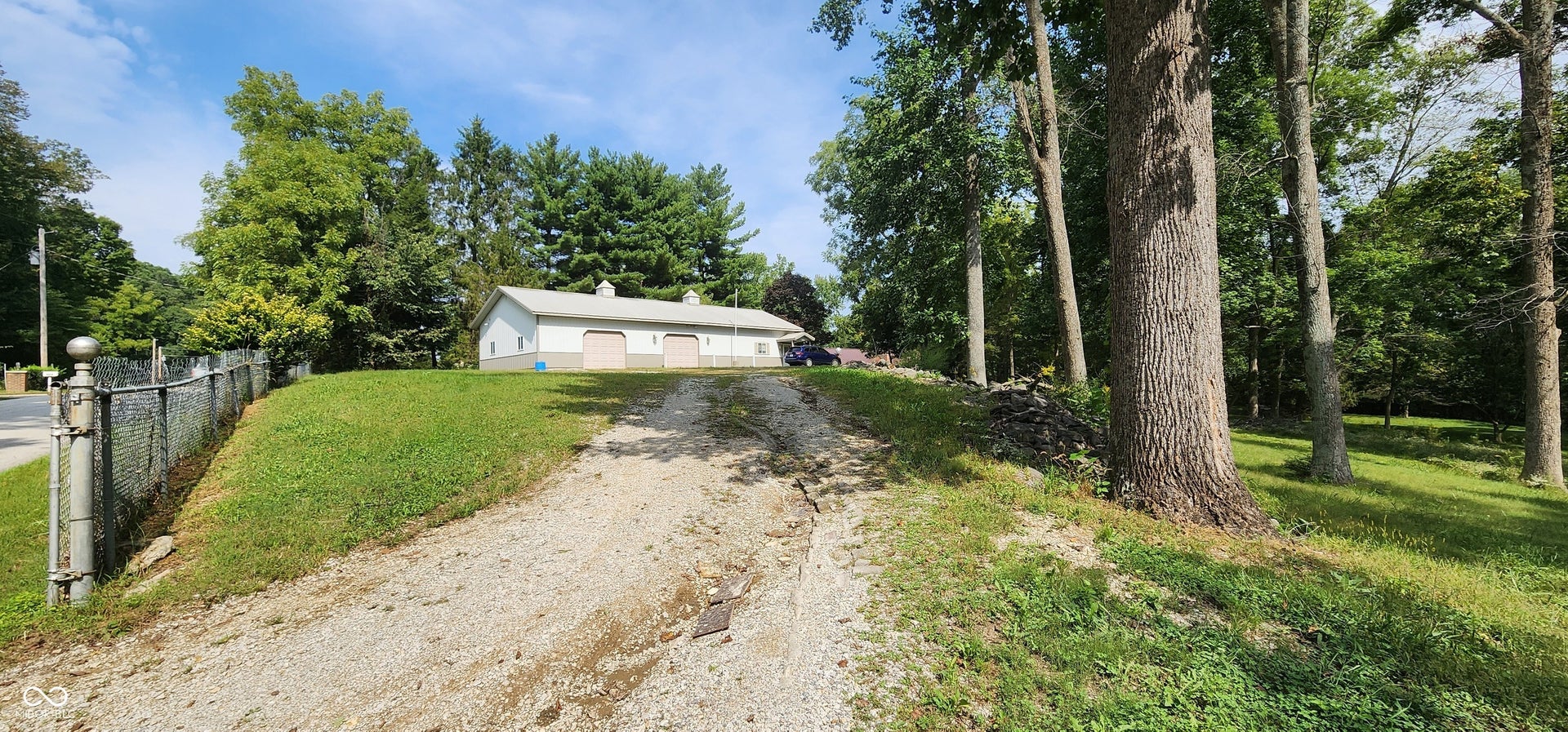 Detached auxiliary building with multiple garage doors, set on a gravel driveway with a chain-link fence