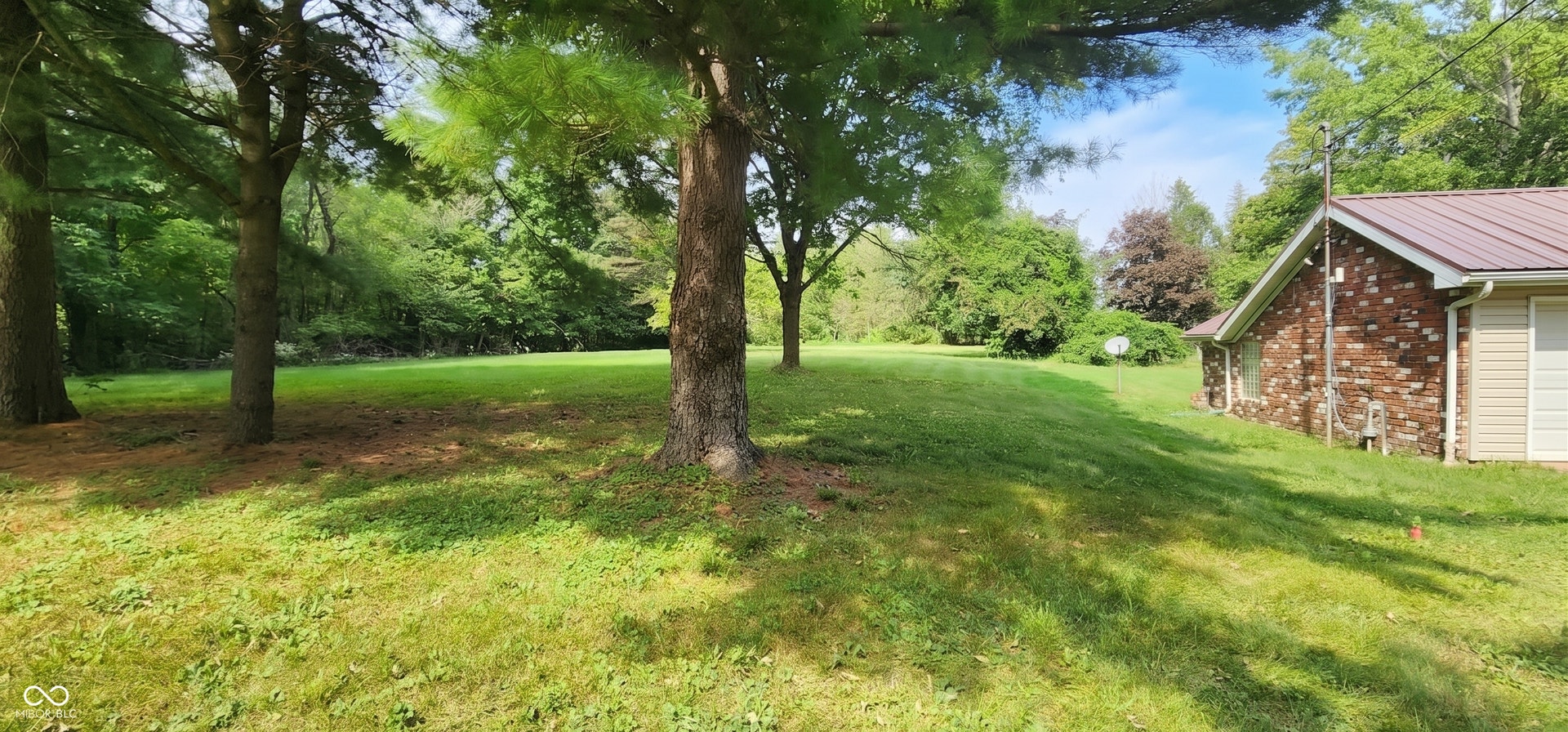 Expansive green lawn with mature trees and a brick-sided structure featuring a metal roof