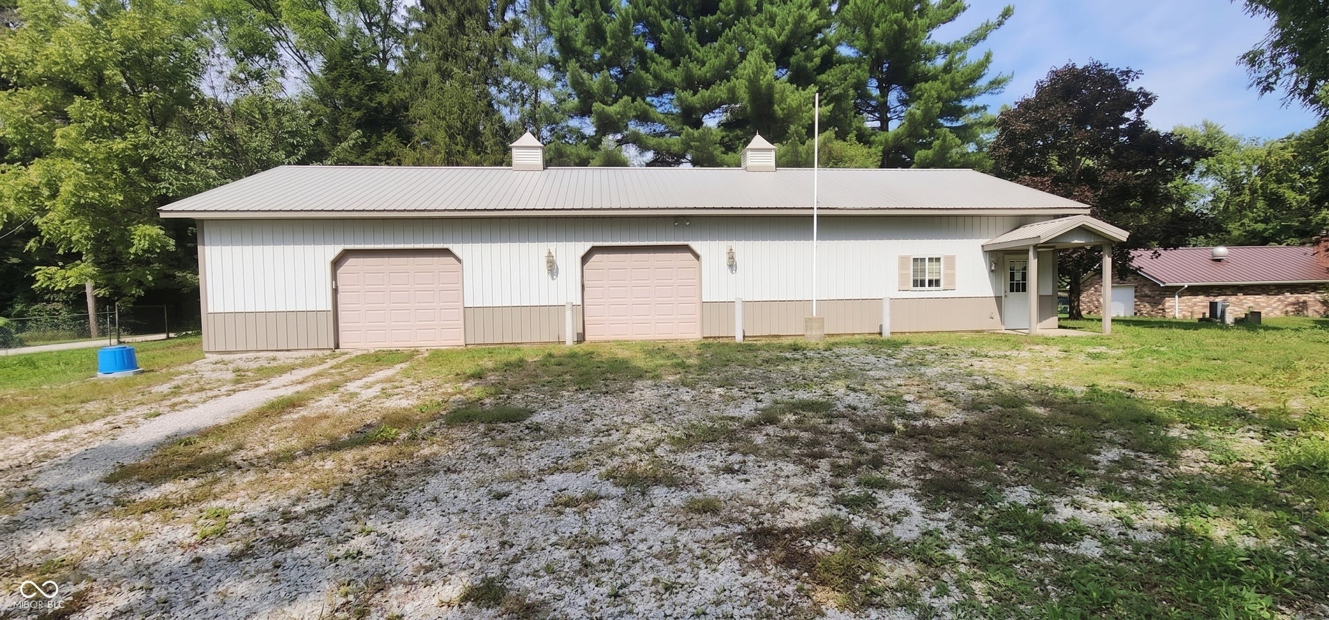 Detached structure featuring a metal roof, two roll-up garage doors, cupolas, and exterior lighting fixtures