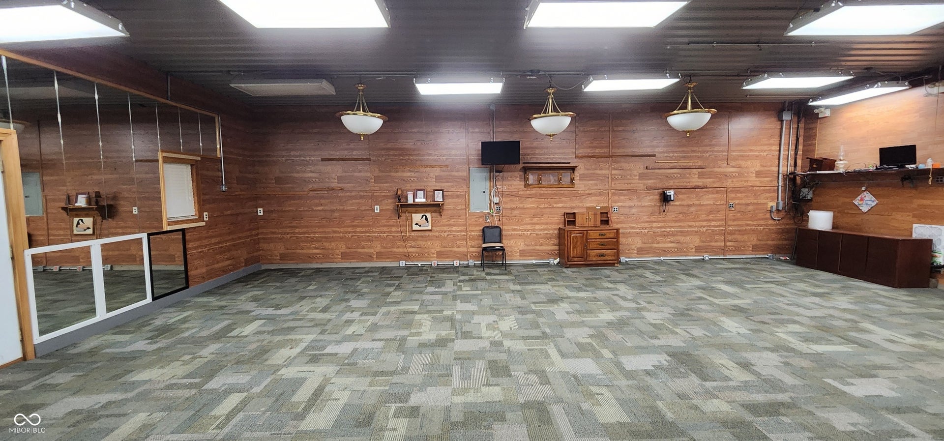 Spacious interior featuring patterned carpet flooring, wood panel wall accents, and multiple overhead light fixtures