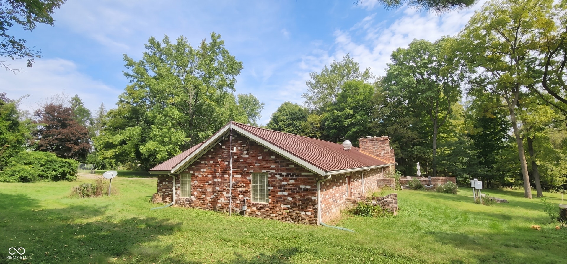 Brick exterior with a brown metal roof, featuring multiple block windows and a prominent brick chimney