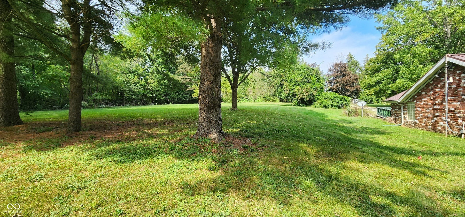 Expansive lawn area with mature trees and a brick exterior structure