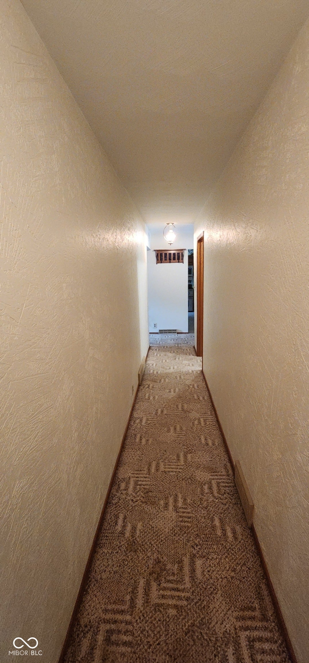 Hallway featuring textured walls, patterned carpet, and a flush-mount light fixture