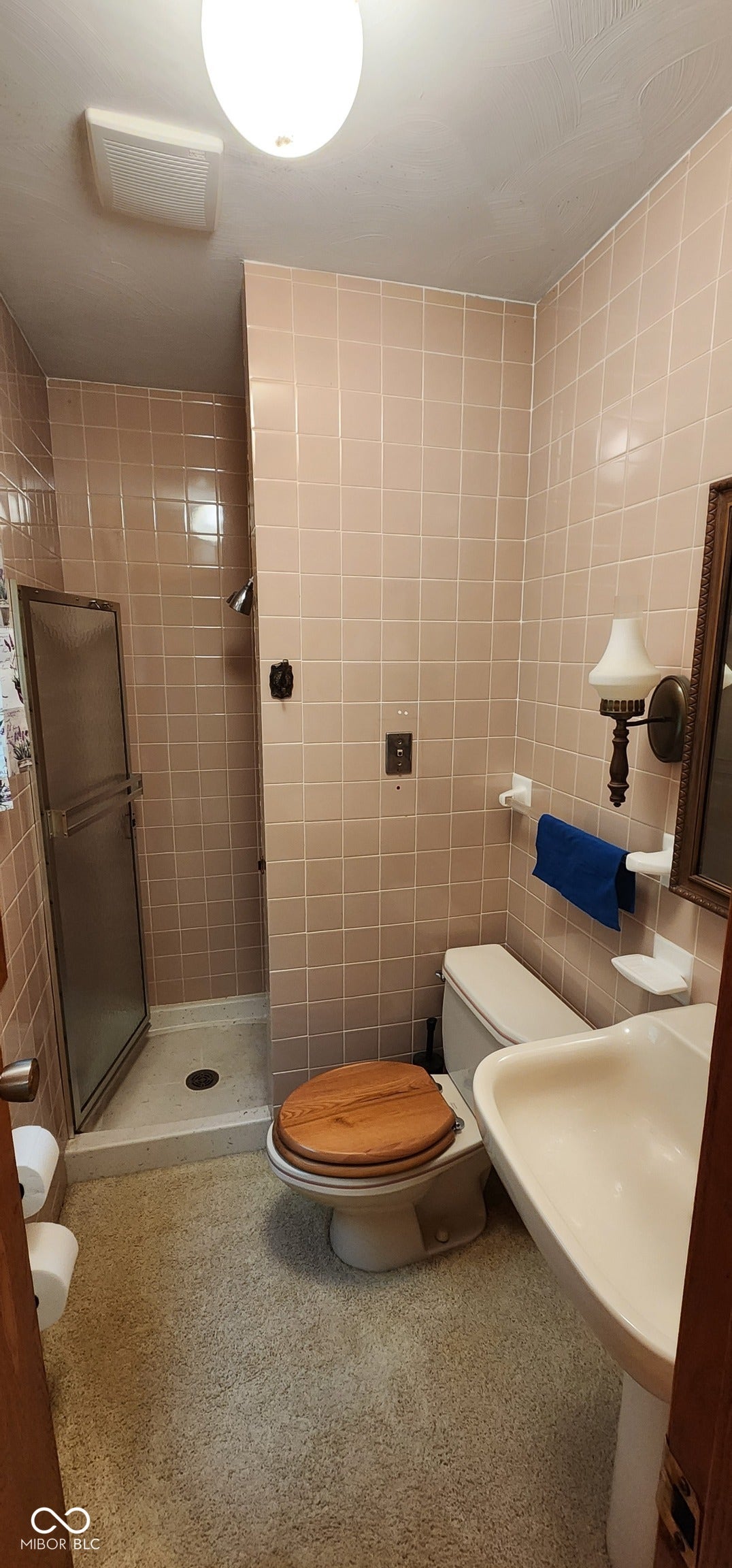 Enclosed shower with a sliding glass door, pedestal sink, toilet, and tiled walls