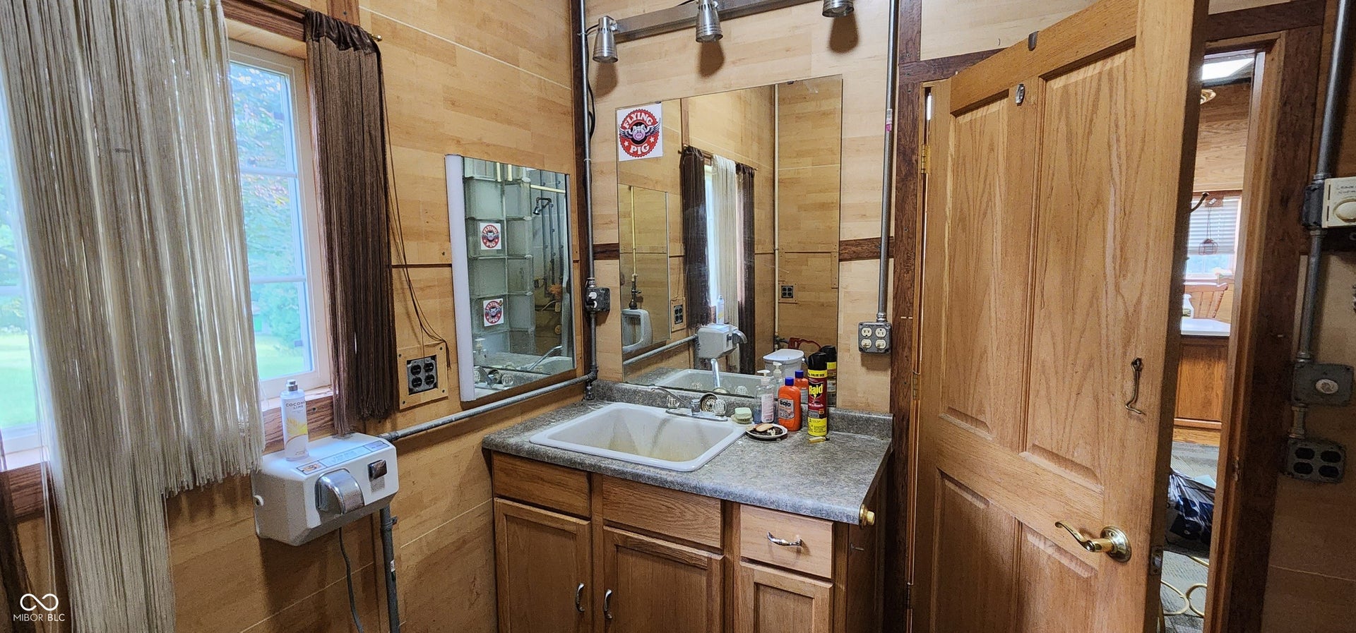 Wood-paneled interior wall, wood-finish vanity with an integrated sink, wall-mounted mirror, and overhead track lighting