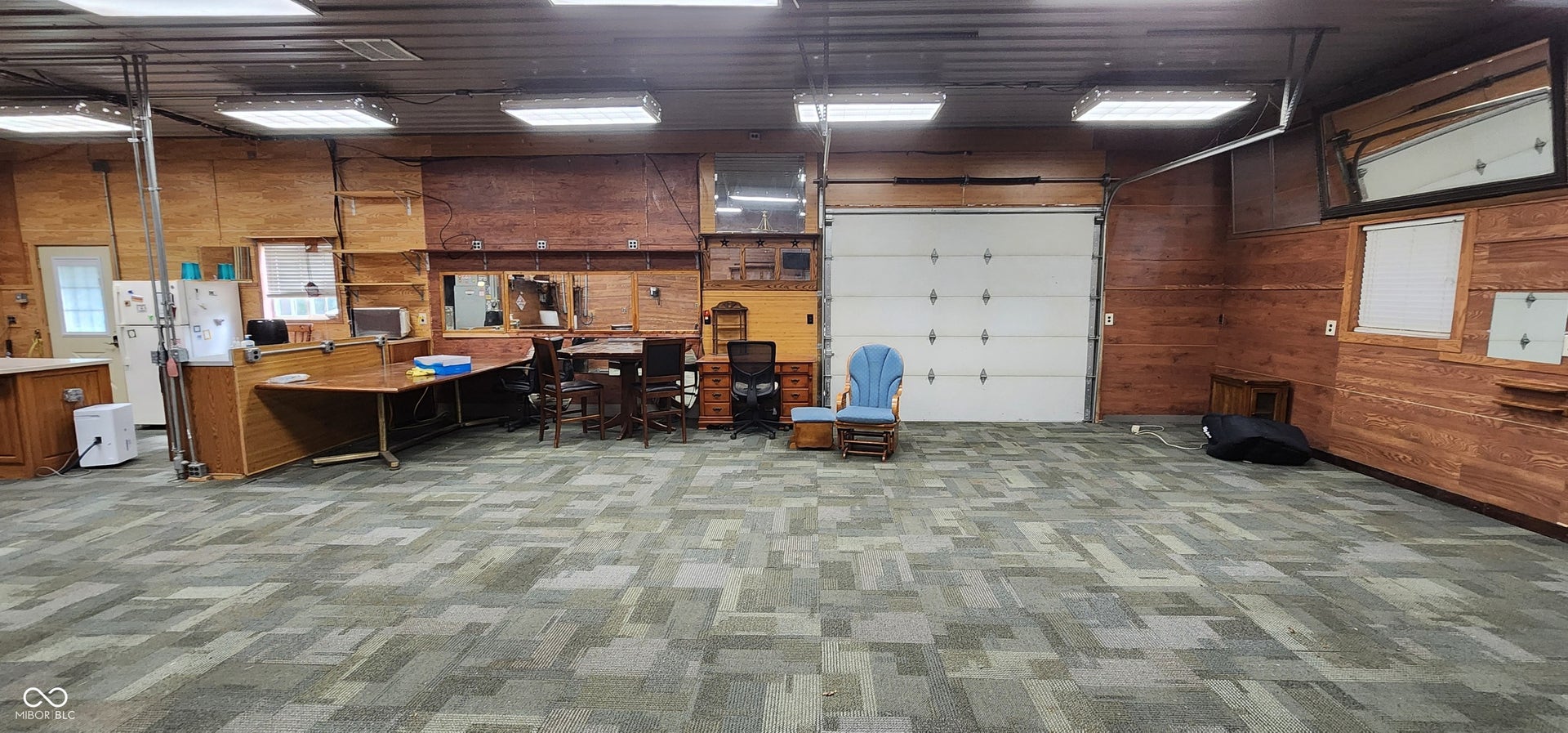 Spacious interior with carpeted flooring, wood-paneled walls, and overhead fluorescent lighting