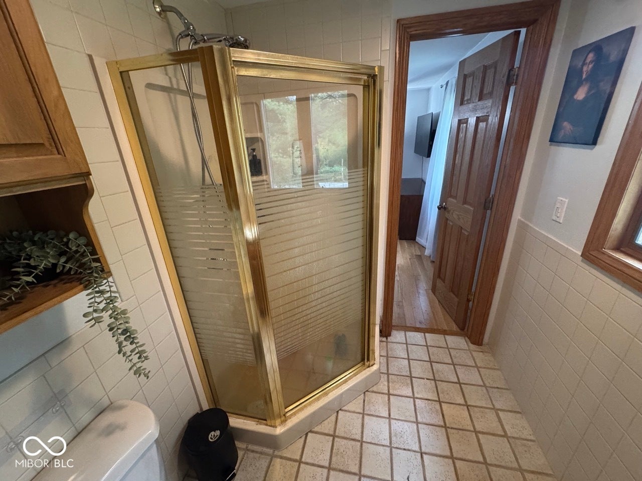 Tiled flooring, shower enclosure with brass-finish frame, tiled wall surround, and wood-finish door with matching trim