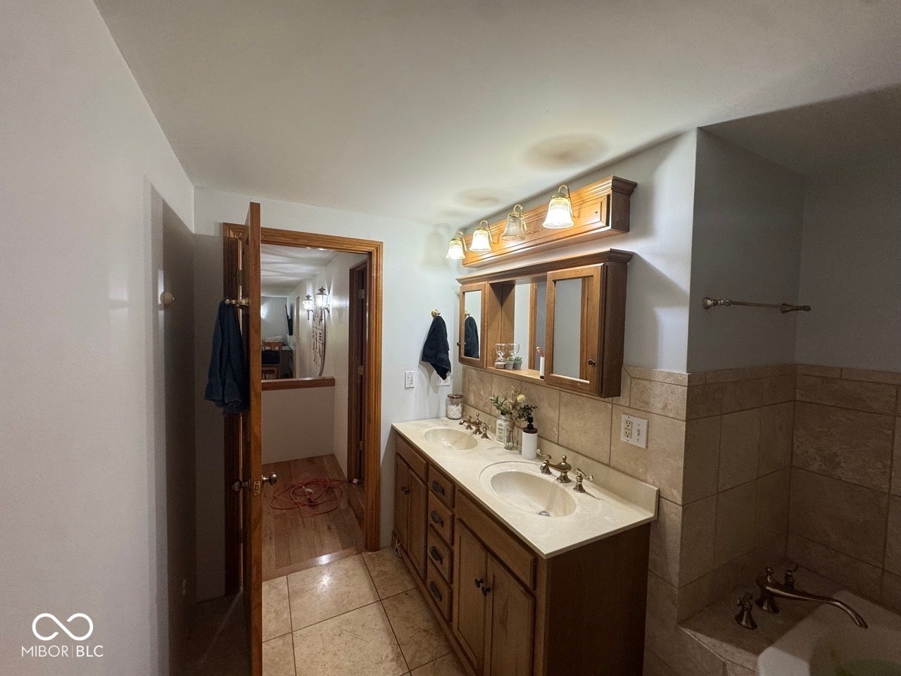 Double vanity with integrated sinks, wood cabinetry, tile flooring, and tiled bath surround