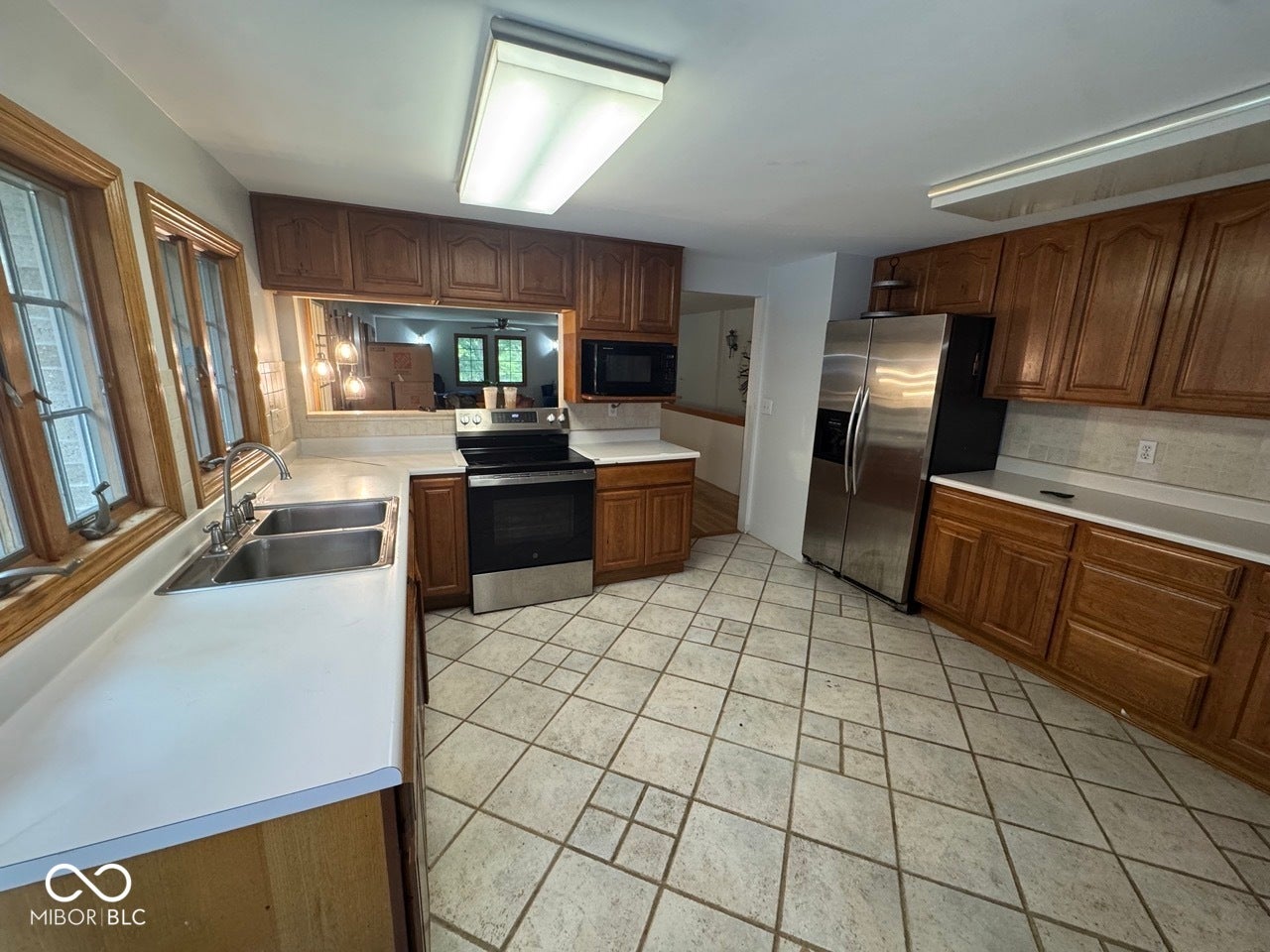 Kitchen featuring wood cabinetry, light-toned countertops, a double basin sink, stainless steel appliances, and patterned tile flooring