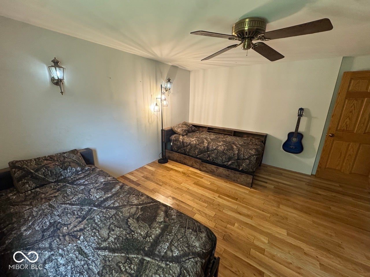 Wood-finish flooring with a ceiling fan, wall sconce, and wood-paneled door