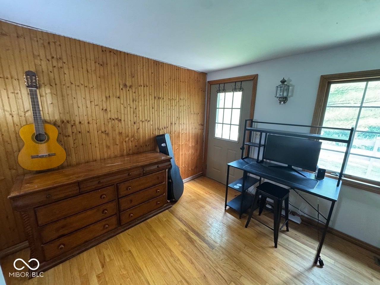 Hardwood flooring, wood panel accent wall, natural light from multiple windows, and a glass-paneled exterior door