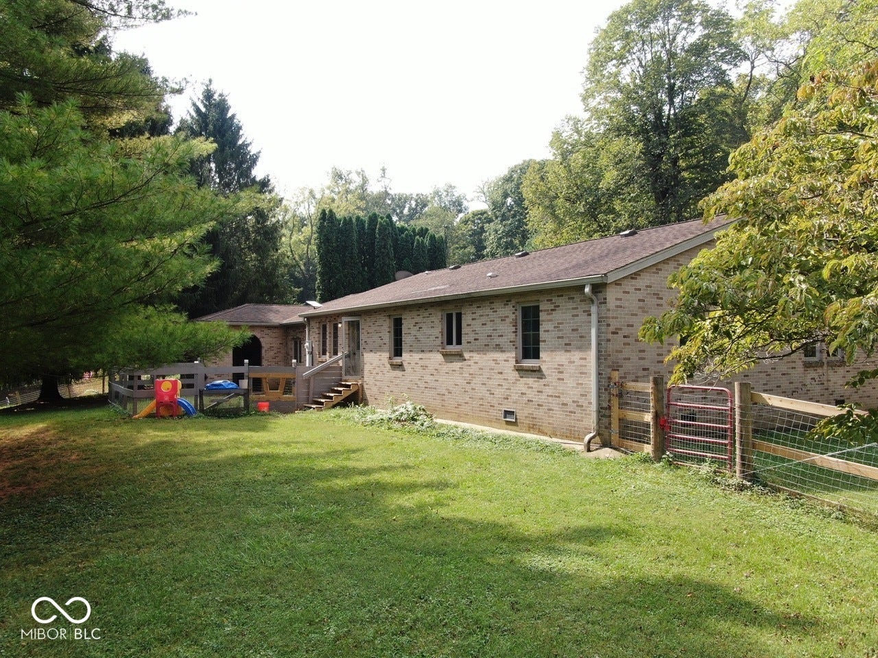 Brick exterior with multiple windows, a wooden deck with railing, and a fenced yard