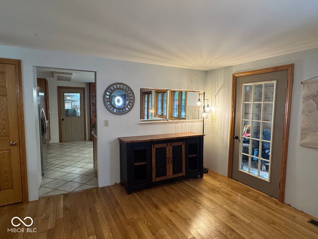 Hardwood flooring, French pane exterior door, wainscoting, and an open doorway to a tiled area