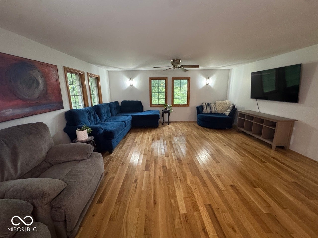 Hardwood flooring, multiple windows with wood trim, ceiling fan, and wall sconce lighting
