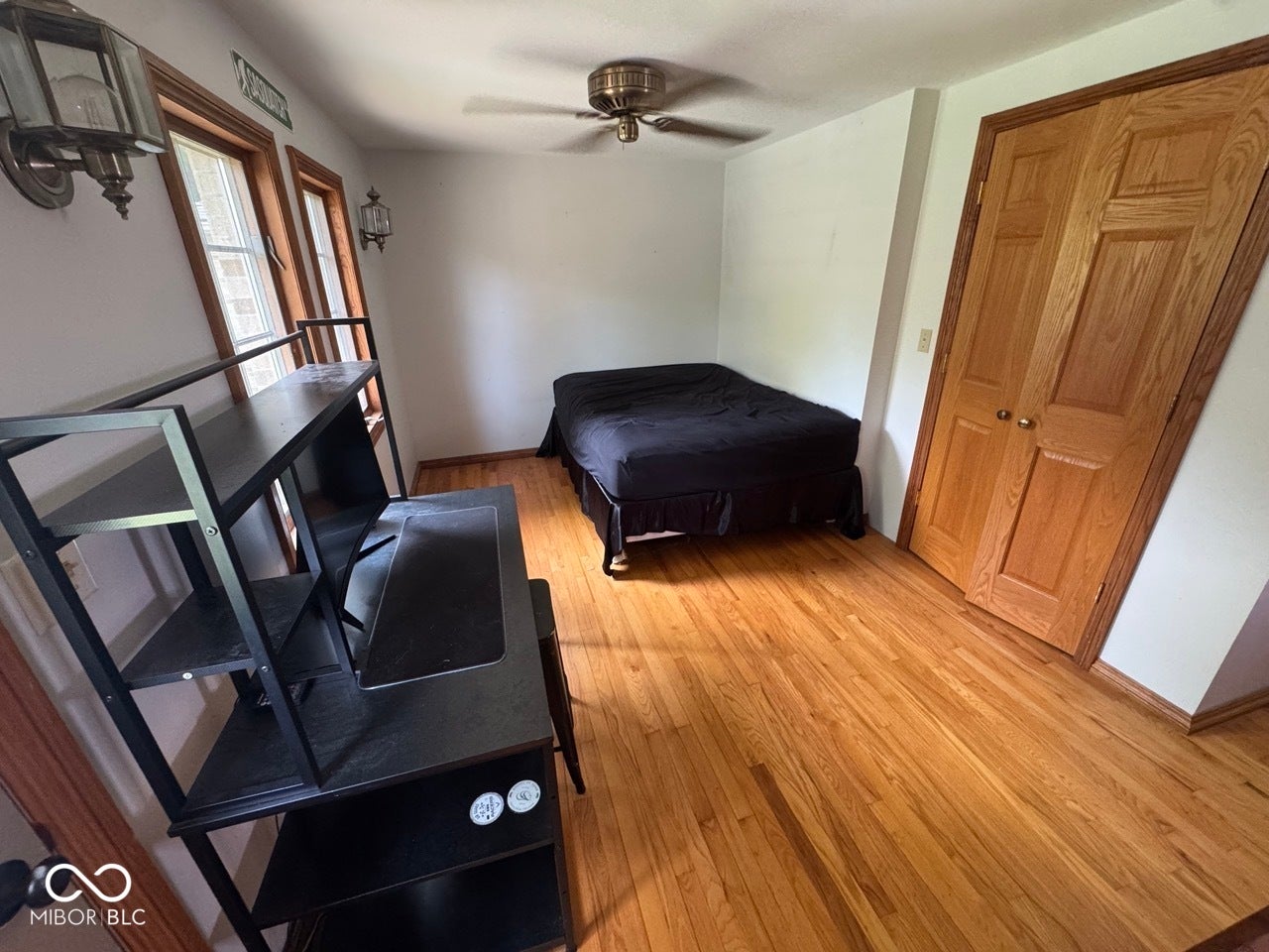 Hardwood flooring, natural wood window trim, two windows, wood bi-fold closet doors, and a ceiling fan
