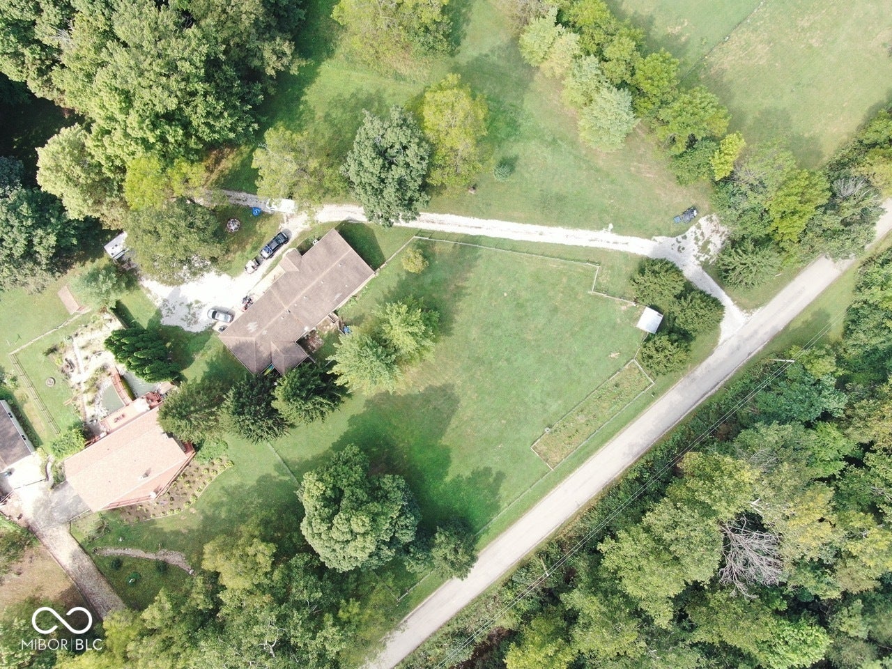 Aerial perspective showcasing the property with a visible roofline, expansive surrounding greenery, and direct road access