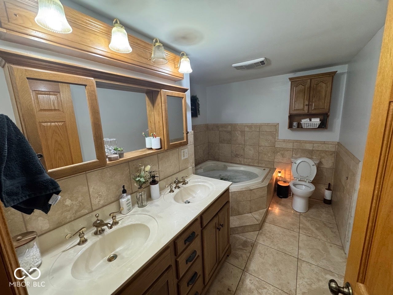 Dual vanity with integrated sinks, corner jetted tub, ceramic tile flooring, and wall-mounted cabinetry
