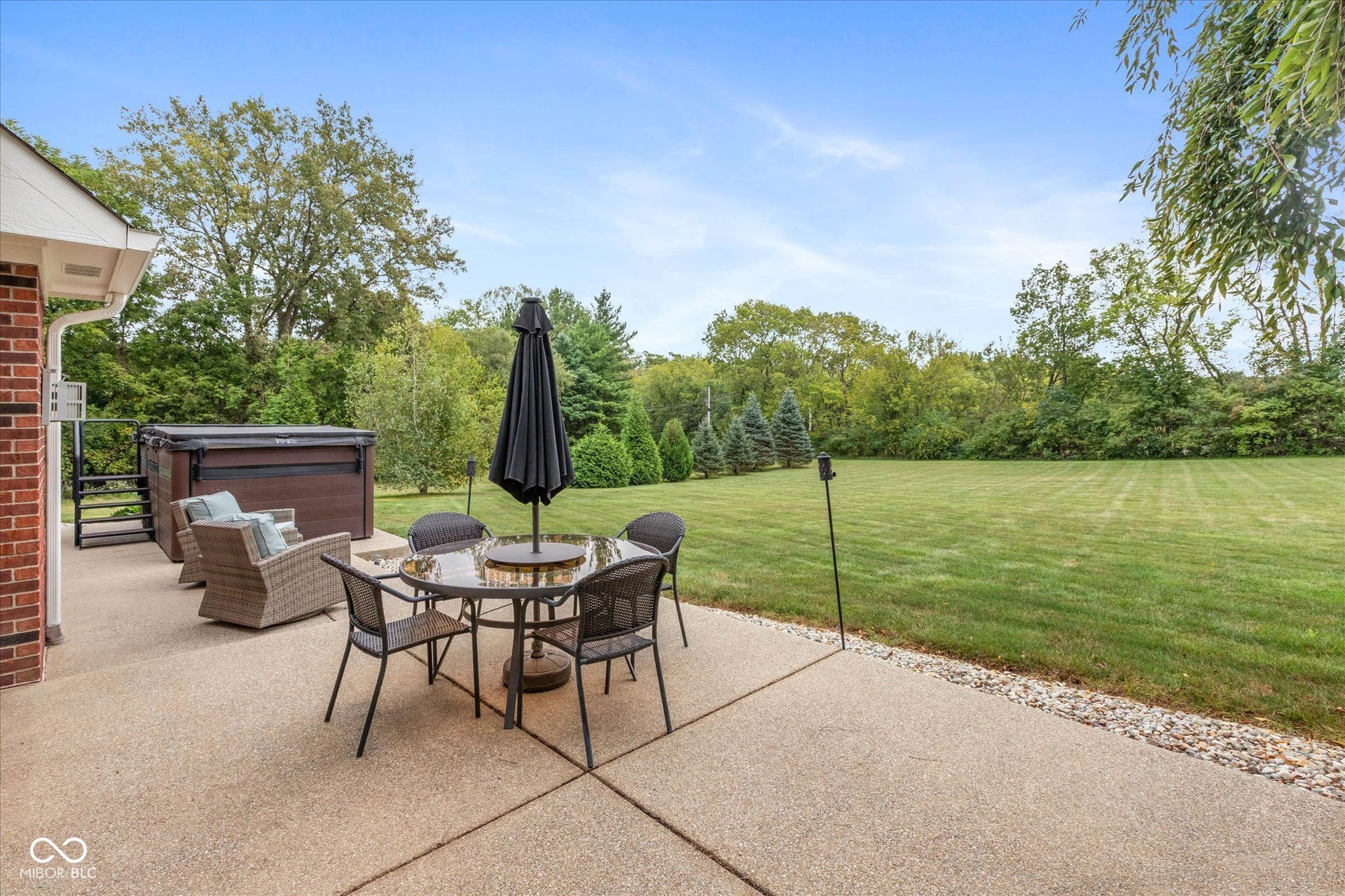 1513 Tottenham, Danville, IN 46122 Expansive concrete patio with a built-in hot tub, providing direct access to a large grass area and mature perimeter trees