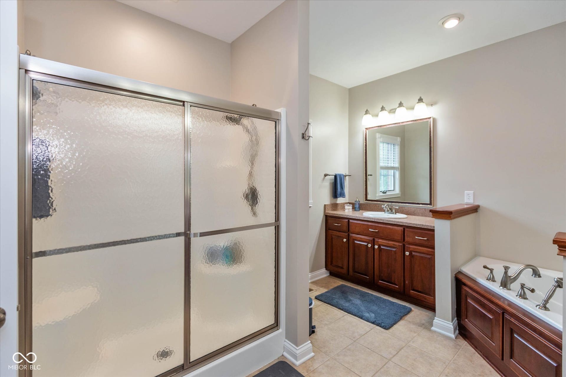 1513 Tottenham, Danville, IN 46122 Tiled bathroom featuring a built-in soaking tub, a dark wood-finish vanity with an integrated sink, a large framed mirror, and a shower with sliding frosted glass doors